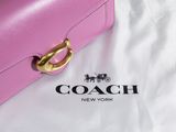 pink coach purse laying on a white sheet with a coach logo on it