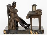 bronze statue of a man sitting at a desk with a lamp on it