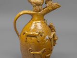 cruche émaillée jaune, ornée d'oiseaux sur le dessus, sur un fond gris