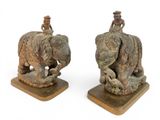 two statues of people riding on top of elephants on wooden bases