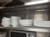 several white plates are stacked on top of a stainless steel shelf