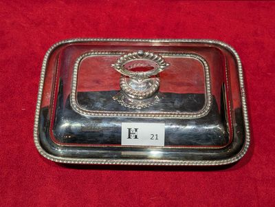 un plat ancien en argent avec un couvercle en verre, posé sur un napperon rouge
