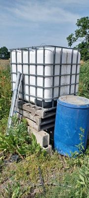a blue barrel sitting in the middle of a field next to a blue barrel