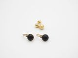 une paire de boucles d'oreilles noires et dorées posées sur une surface blanche