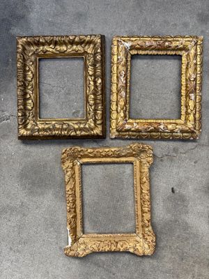 trois cadres dorés posés sur une surface en béton