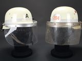 une paire de casques blancs avec des visières transparentes, posés sur des supports, sur fond noir