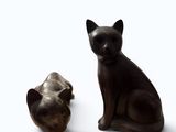 two statues of cats sitting next to each other on a white surface