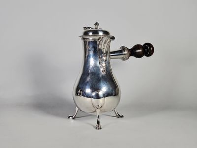 une cafetière ancienne en métal argenté, munie d'une anse et posée sur un socle