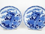 two blue and white plates with peacocks and flowers on them