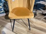 une chaise en velours jaune aux pieds noirs, dans une pièce aux murs bleus, avec une table en verre