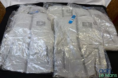 trois chemises blanches emballées dans des sacs en plastique, posées sur une table noire