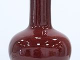 un vase rouge avec un couvercle doré posé sur une table blanche