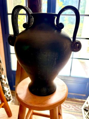 un vase noir posé sur un tabouret en bois devant une fenêtre