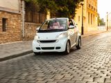 a small white car driving down a cobblestone street