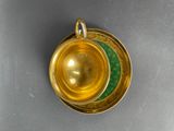 a gold cup and saucer with a green saucer on it