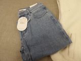 two pairs of jeans on a bed with a price tag
