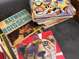 several children ' s books are stacked on a table next to a red suitcase