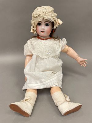 une vieille poupée vêtue d'une robe blanche et d'un chapeau, assise sur une surface grise