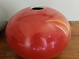 a red vase sitting on a wooden table next to a white vase