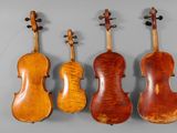a group of four antique violin ' s on a grey background