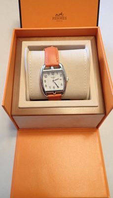 une boîte orange contenant une montre, posée sur une surface blanche