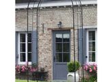Une arche en métal noir se dresse devant un bâtiment en briques