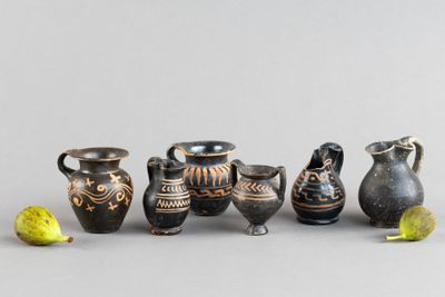 Plusieurs vases et une figurine sont alignés sur une surface grise