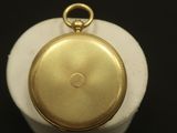 une image représentant une montre de poche en or posée sur un socle blanc