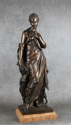 une statue en bronze représentant une femme tenant un chien, posée sur un socle en bois