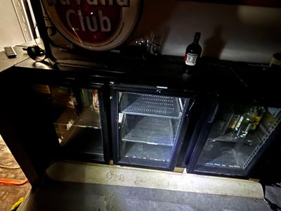une porte vitrée ouverte laissant entrevoir un réfrigérateur à boissons