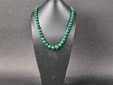 a green beaded necklace on a black mannequin