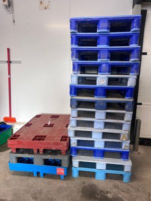 une pile de palettes en plastique dans un garage, à côté d'une pile de palettes bleues et rouges