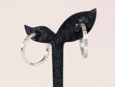 une paire de boucles d'oreilles créoles en argent posées sur un support noir, sur fond blanc