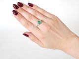 a woman ' s hand holding a ring with a green stone on it
