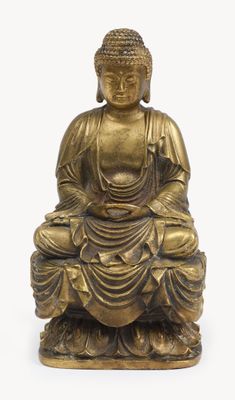 a gold statue of a buddha sitting on a white surface