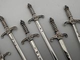 five silver swords are lined up in a row on a white surface