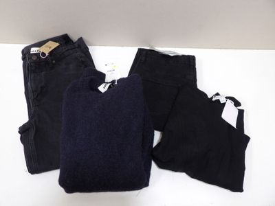 deux paires de pantalons noirs et un pull noir posés sur une table blanche