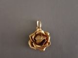 un gros plan d'un pendentif en forme de rose dorée posé sur une surface blanche