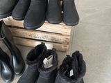 Plusieurs paires de bottes noires sont alignées sur une caisse en bois