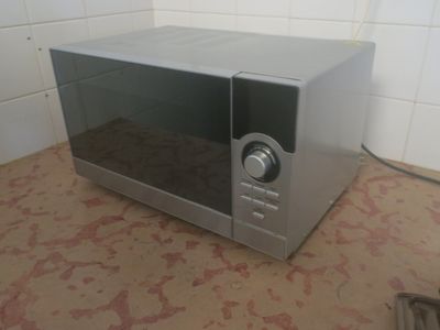 un micro-ondes argenté posé par terre dans une cuisine