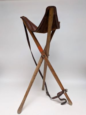 une chaise en bois avec une assise en cuir et deux pieds croisés