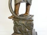 une statue en bronze représentant un homme avec un serpent, assis sur un rocher