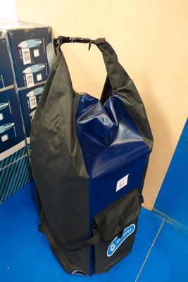 un sac noir posé sur un sol bleu, à côté d'une pile de cartons