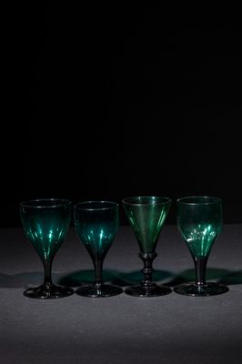 four green wine glasses are lined up in a row on a table