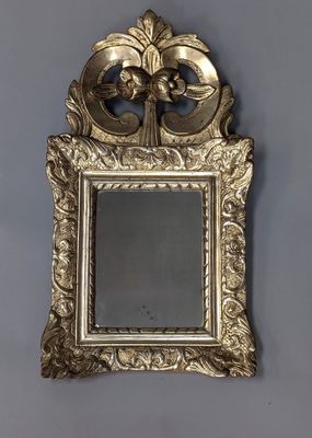 un miroir au cadre doré ouvragé accroché à un mur gris