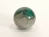 une boule de marbre verte et blanche posée sur une surface blanche, avec un fond blanc