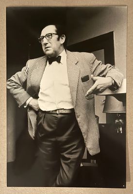 photographie en noir et blanc d'un homme en costume et nœud papillon, adossé à un mur