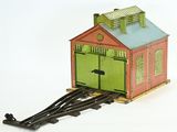 un petit train miniature avec une porte verte et un bâtiment rouge