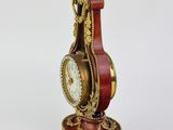 a red and gold clock on a stand on a white surface
