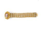 a close up of a gold bracelet with a pink stone in the center